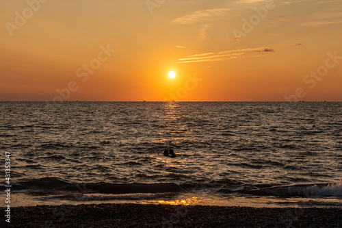 Fototapeta Naklejka Na Ścianę i Meble -  Beautiful orange sunrise is on the beach by the sea with black ship silhouettes and a group of swimming people