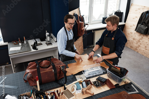 leather craftsmen working making measupenets in patterns at table in workshop studio