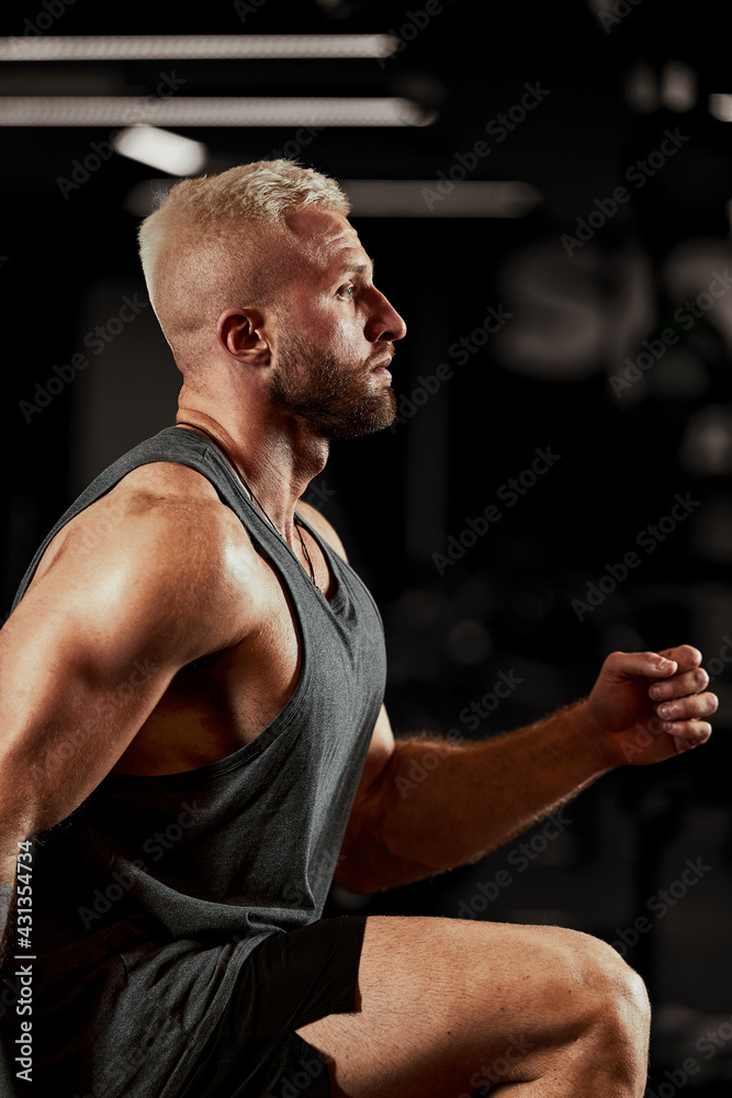 Sexy muscular men using the platform for his legs on a dark colorful background of gym. Sexy muscular men using the platform for his legs on a dark colorful background of gym.