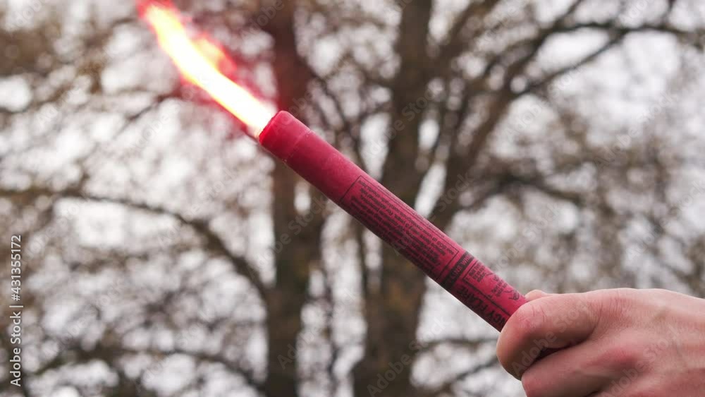 Red signal light in a man's hand on the background of nature outside. Close-up. Burning fire. A signal for help Red signal light in a man's hand on the background of nature outside. Close-up. Burning fire. A signal for help