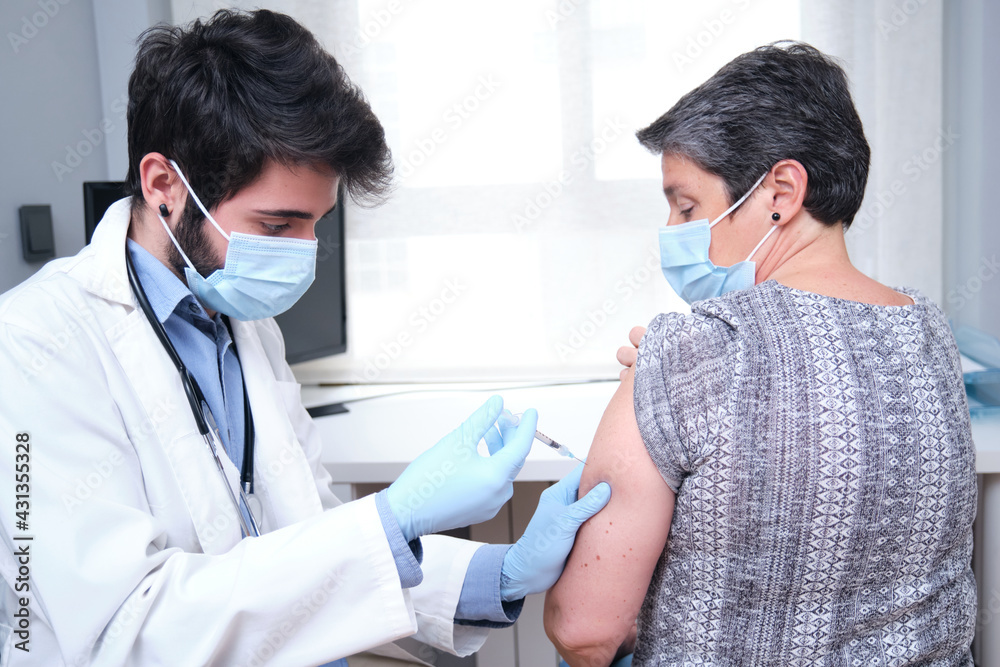 Obraz premium Doctor vaccinating mature woman patient in clinic. Nurse holding syringe before inject Covid-19 or coronavirus vaccine.