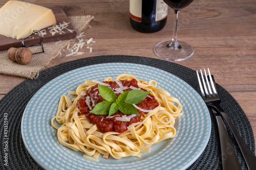 dish with noodles topped with tomato sauce, with a glass of sparkling red wine