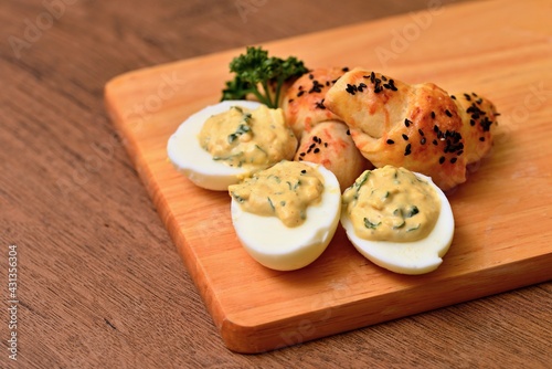 Eggs mimosa cheese mini-croissant on a wooden board. Arranged eggs and pastries with a sprig of curly parsley. Eggs stuffed with cream, homemade pastries rolls on a wooden background.