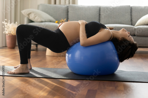 Calm young Caucasian woman lie on fitball do morning gymnastics training at home. Active sporty female follow healthy lifestyle during pregnancy, exercise with stretching or pilates. Sports concept.
