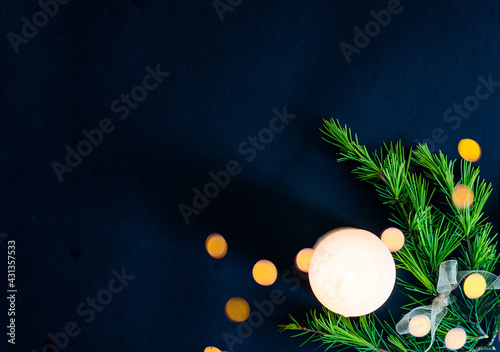 Scena con una candela bianca accesa circondata da rami di abete e legati con un fiocco dorato e con delle luci sfuocate sullo sfondo nero, con spazio per scrivere. Condoglianze. Auguri.