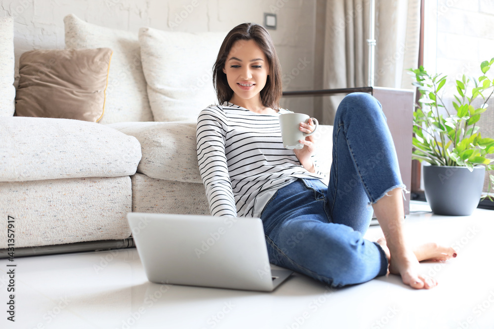 Pretty woman working with laptop while sitting on floor at home and drinking coffee. Pretty woman working with laptop while sitting on floor at home and drinking coffee.