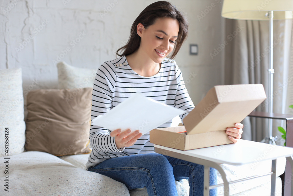 Beautiful young woman is holding cardboard box and unpacking it sitting on sofa at home. Beautiful young woman is holding cardboard box and unpacking it sitting on sofa at home.