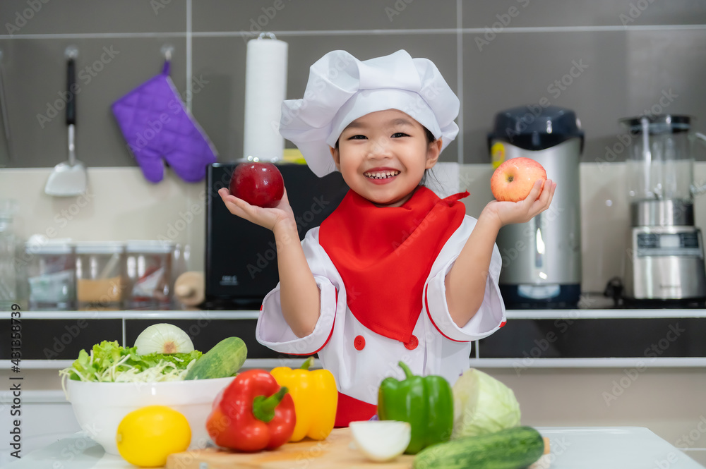 Cute asian girl wear chef uniform with a lot of vegatable on the table in the kitchen room,Make food for eat dinner,Funny time for kids Cute asian girl wear chef uniform with a lot of vegatable on the table in the kitchen room,Make food for eat dinner,Funny time for kids
