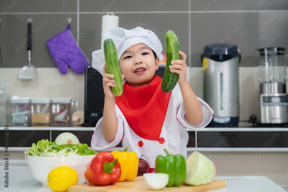 Cute asian girl wear chef uniform with a lot of vegatable on the table in the kitchen room,Make food for eat dinner,Funny time for kids Cute asian girl wear chef uniform with a lot of vegatable on the table in the kitchen room,Make food for eat dinner,Funny time for kids