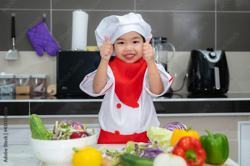 Cute asian girl wear chef uniform with a lot of vegatable on the table in the kitchen room,Make food for eat dinner,Funny time for kids Cute asian girl wear chef uniform with a lot of vegatable on the table in the kitchen room,Make food for eat dinner,Funny time for kids