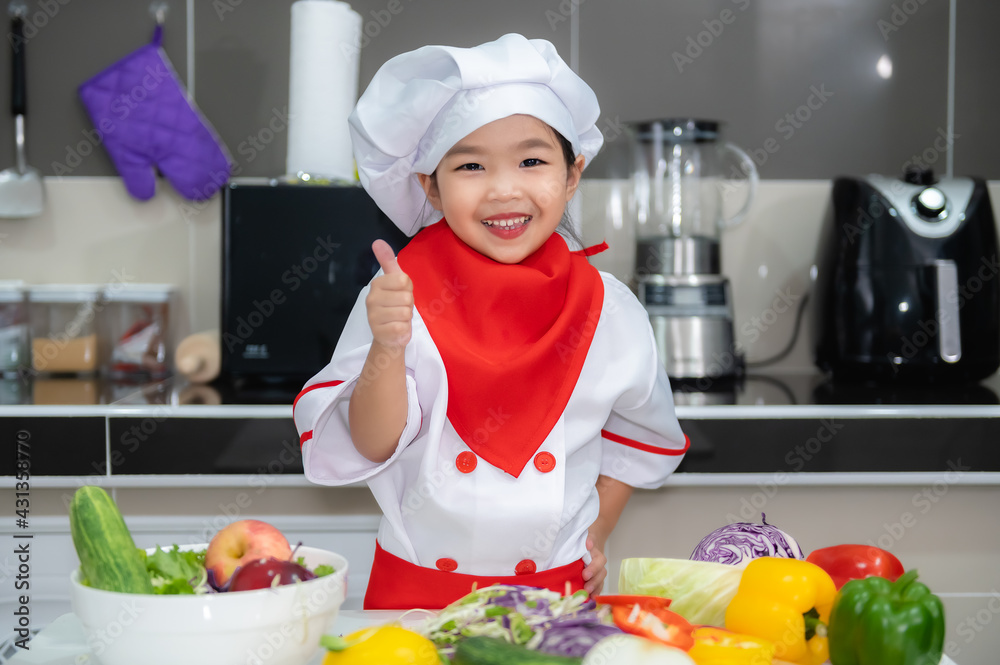 Cute asian girl wear chef uniform with a lot of vegatable on the table in the kitchen room,Make food for eat dinner,Funny time for kids Cute asian girl wear chef uniform with a lot of vegatable on the table in the kitchen room,Make food for eat dinner,Funny time for kids