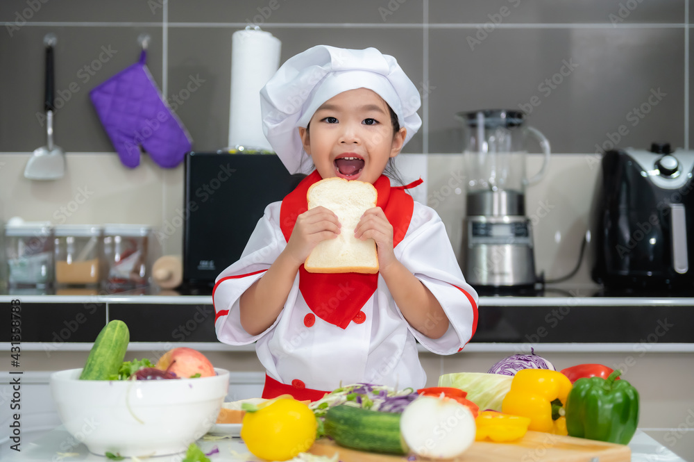 Cute asian girl wear chef uniform with a lot of vegatable on the table in the kitchen room,Make food for eat dinner,Funny time for kids Cute asian girl wear chef uniform with a lot of vegatable on the table in the kitchen room,Make food for eat dinner,Funny time for kids