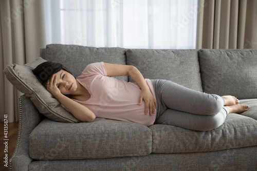 Unwell young Caucasian woman lying on couch touch baby bump feel unhealthy suffer from pain ache. Tired female relax on sofa touch baby bump have health problems during pregnancy. Healthcare concept.