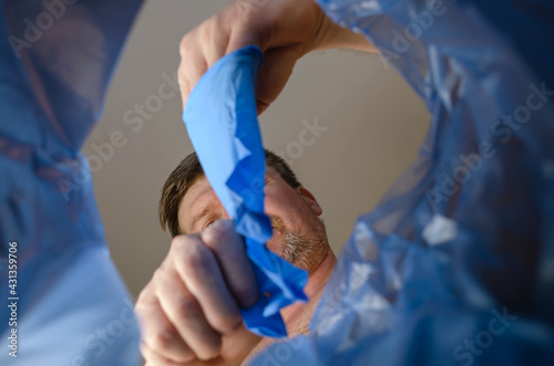 A hand tosses blue medical gloves into a trash can.