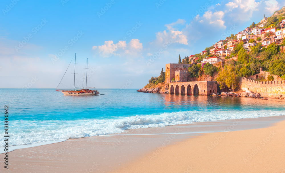 Fototapeta premium Beautiful sandy beach and soft turqoise Mediterranean sea wave - Landscape of ancient shipyard near of Kizil Kule tower - Alanya peninsula, Turkey