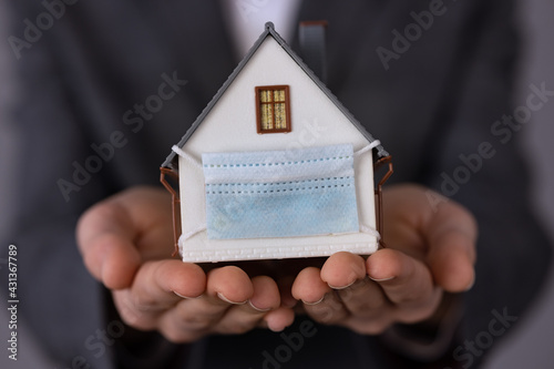 Businesswoman holding model house wearing protective mask in hands