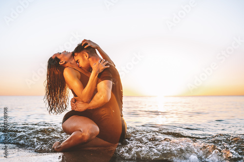 Happy young fit couple embrace each other with love in the sea or ocean at summer sunset. Romantic mood, tenderness, relationship, vacation concept. photo