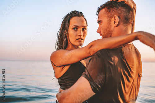 Fit couple in sea or ocean hug each other with love at summer sunset. Romantic mood, tenderness, relationship, vacation concept. Female look at camera