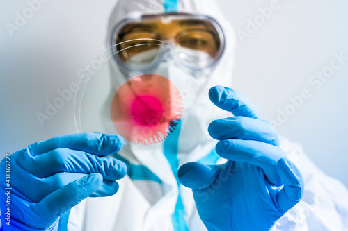 Vaccine researcher with protective clothing in the laboratory with microscope slides and Covid 19 positive blood. Lab technician with a blood sample with a new Coronavirus mutation or variant.