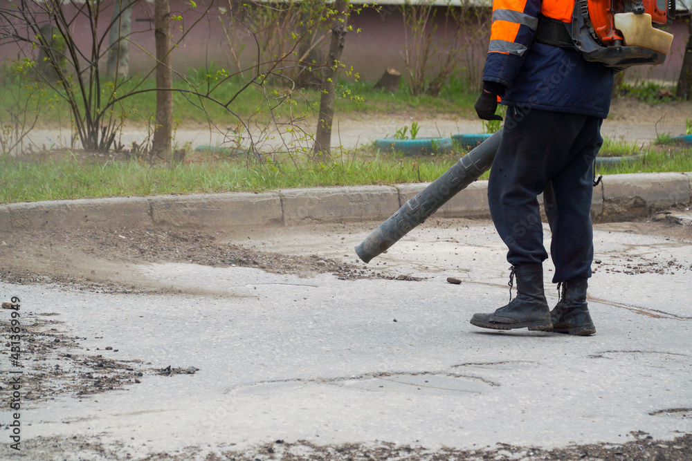 A road worker cleans the asphalt from small stones and other debris with a blower pipe. A road worker cleans the asphalt from small stones and other debris with a blower pipe.