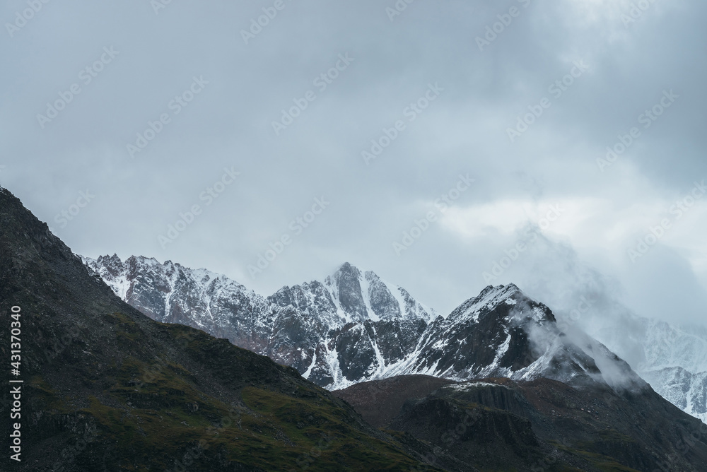 Atmospheric alpine landscape with great mountain peaked top with snow in low clouds. Dramatic mountain scenery with sharp pinnacle in overcast weather. Awesome view to snowy pointy peak in cloudy sky. Atmospheric alpine landscape with great mountain peaked top with snow in low clouds. Dramatic mountain scenery with sharp pinnacle in overcast weather. Awesome view to snowy pointy peak in cloudy sky.