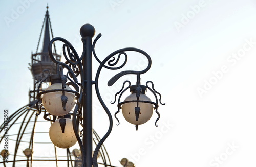 Electric street lamp exclusive shape, metal and glass, close-up against a blue cloudy sky © Анатолий Мироненко