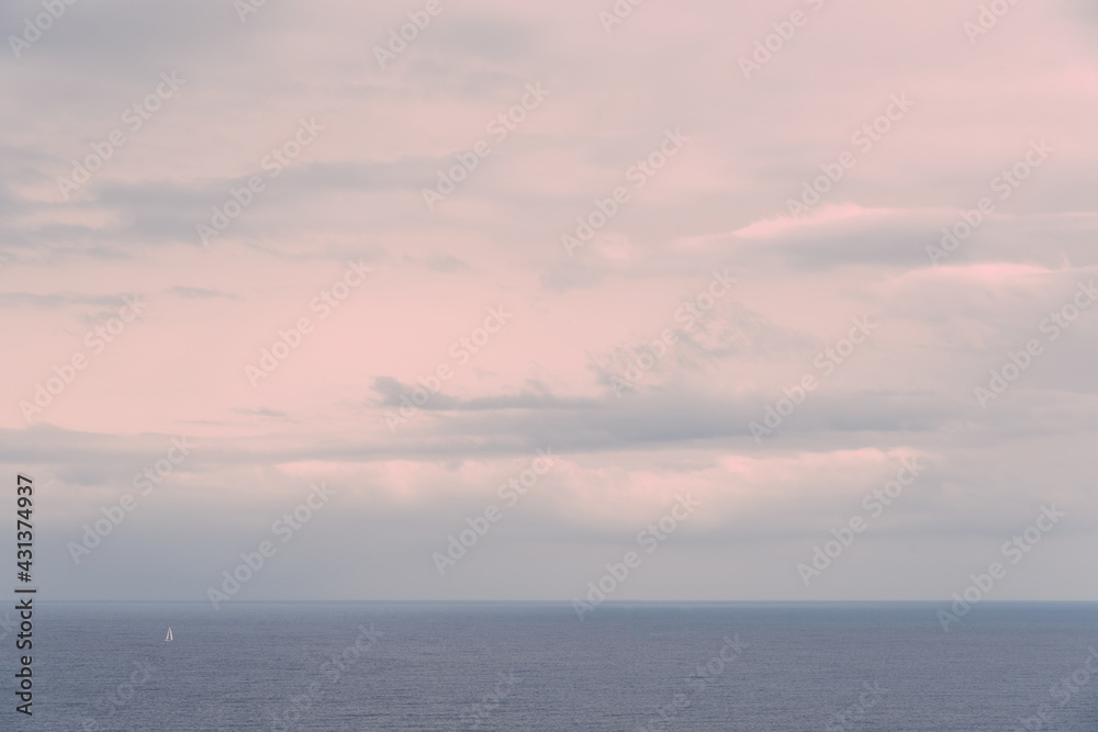 View of the Mediterranean Sea after the rain at sunset and a small sailboat crosses the frame.