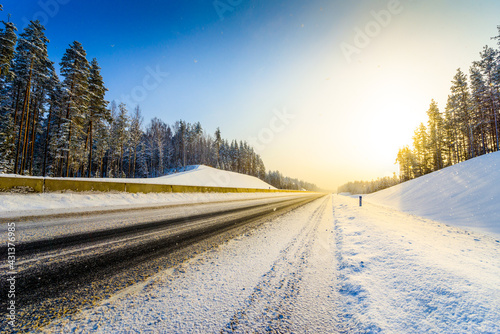 Sunrise on a clear winter morning, empty highways in snow. View from the side of the road. Coniferous forest. Russia, Europe. Beautiful nature.