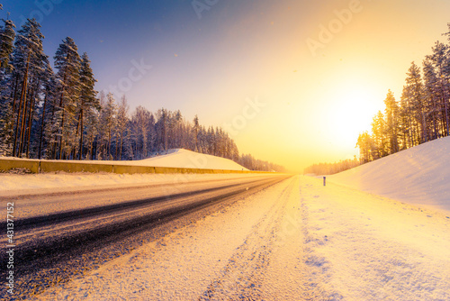 Sunrise on a clear winter morning, empty highways in snow. View from the side of the road. Coniferous forest. Russia, Europe. Beautiful nature.