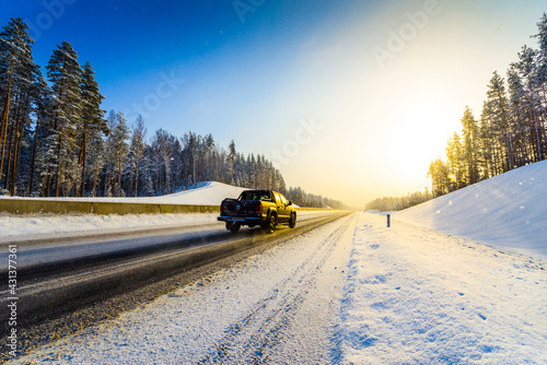 Sunrise on a clear winter morning, pickup rides on the highways in the snow. View from the side of the road. Coniferous forest. Russia, Europe. Beautiful nature. © Georgii Shipin