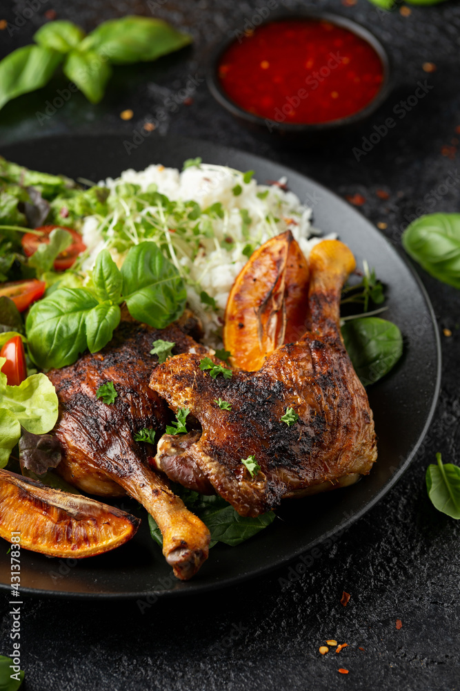 Slow cooked aromatic duck legs with basmati rice and side salad served with orange wedges on black plate Slow cooked aromatic duck legs with basmati rice and side salad served with orange wedges on black plate