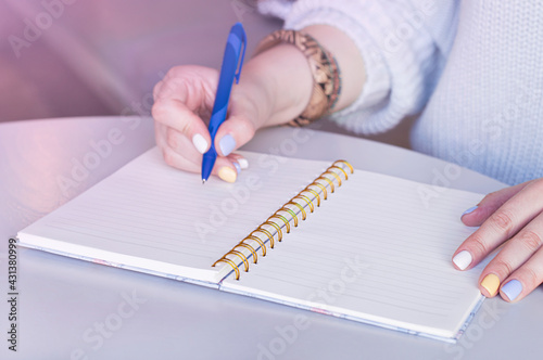 Woman writing in spiral notepad placed on desktop