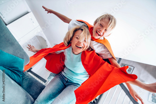 Child and mother in superhero costume playing together at home - Happy son and mom having fun in living room - Family concept photo