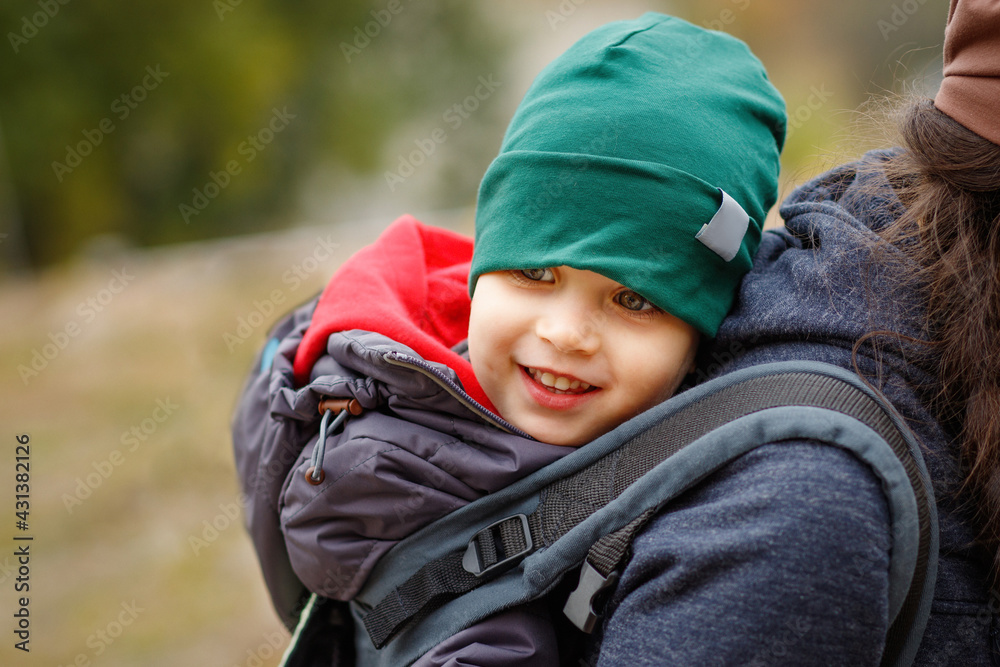 A smiling boy travels behind his mother in a baby carrier A smiling boy travels behind his mother in a baby carrier
