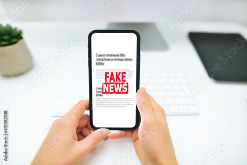 Woman is holding smartphone and reading fake news on internet. Propaganda, misinformation and hoax concept.