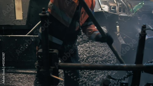 Road workers spread the asphalt with a shovel in front of an asphalt paver. Repair of a city road at night. Road construction works.