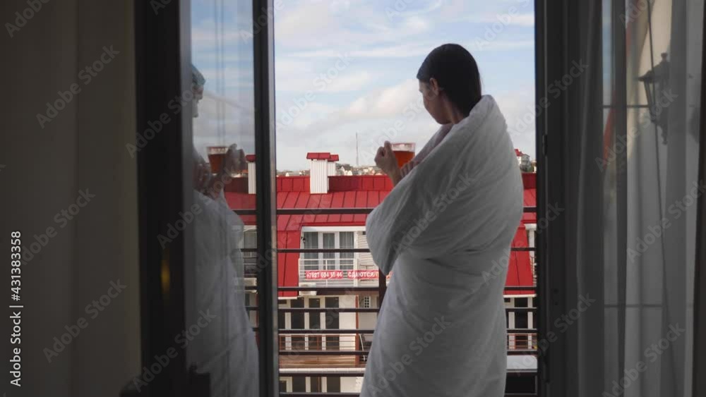 woman in a white blanket stands in the doorway with a cup of tea woman in a white blanket stands in the doorway with a cup of tea