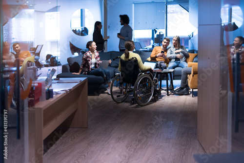 Office workers and handicaped person in a wheelchair discussing business moments in a modern office. Disability and business concept