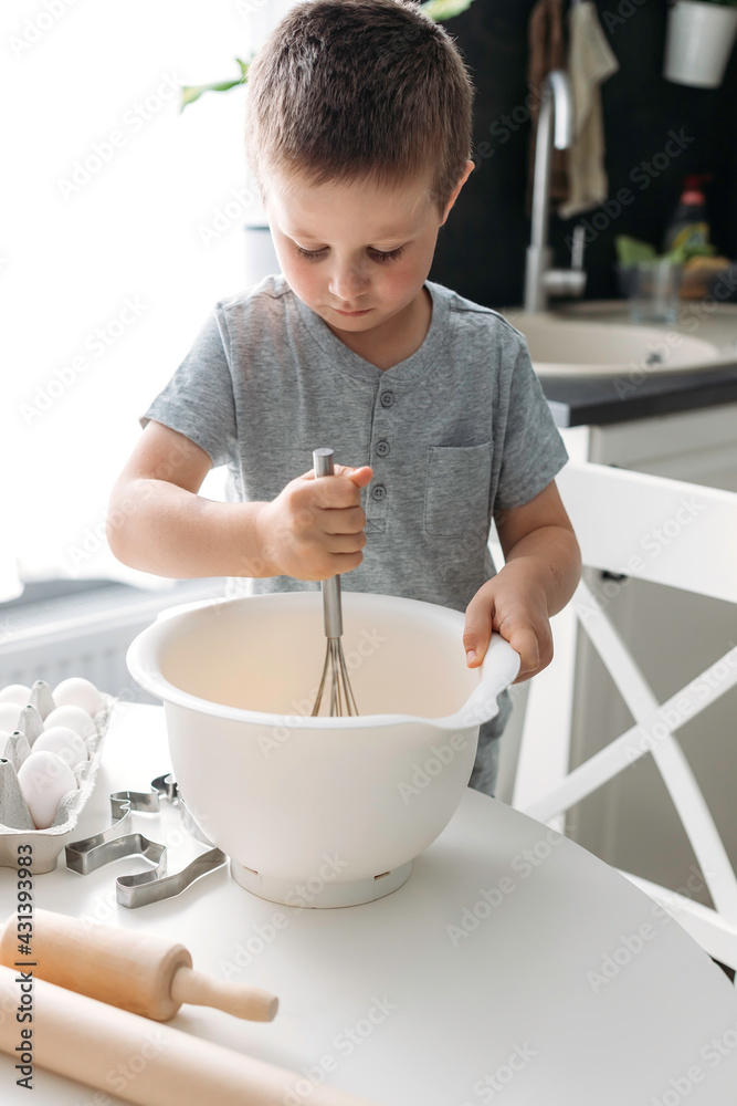 Cute caucasian boy bakes Christmas cookies or gingerbread cookies at home in the kitchen. Real authentic moments of life. Christmas or holiday preparation concept Cute caucasian boy bakes Christmas cookies or gingerbread cookies at home in the kitchen. Real authentic moments of life. Christmas or holiday preparation concept