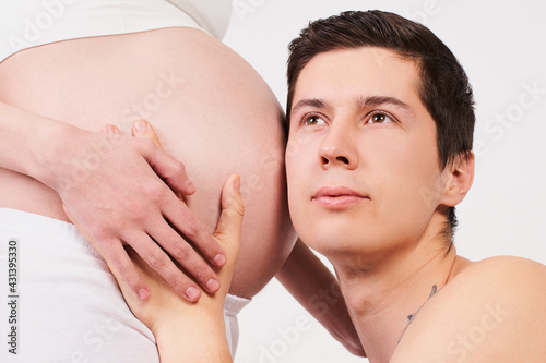 Close-up, a young happy husband listens to the belly of his pregnant wife.