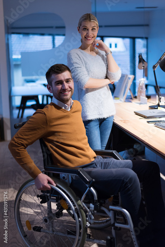 Man in wheelchair and his is female colleague working in the modern co-working office