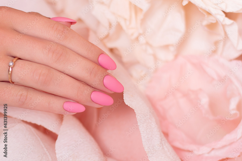 Female hand with wedding manicure nails, pink gel polish, on paper flowers background