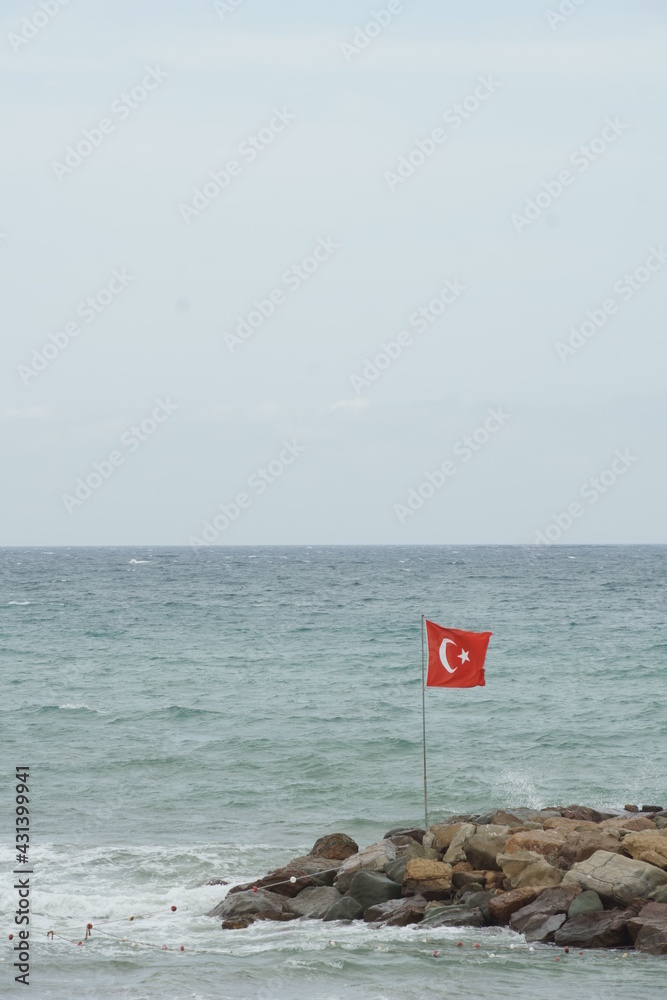 Turkish flag on the flag pole over the rocky pier Turkish flag on the flag pole over the rocky pier