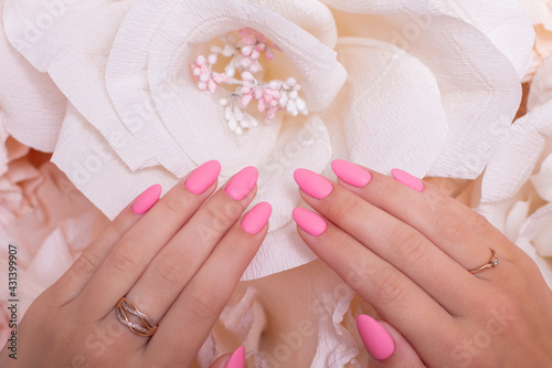 Female hands with wedding manicure nails, pink gel polish, on paper flowers background
