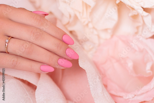 Female hand with wedding manicure nails  pink gel polish  on paper flowers background