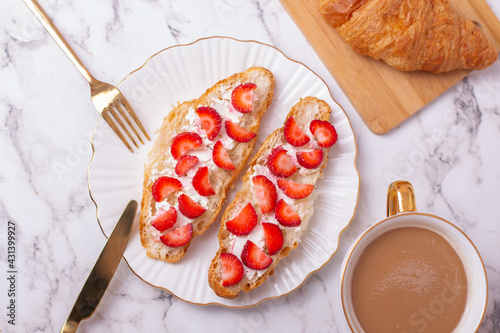 Coffee cup and sweet croissant with fresh strawberry on white table