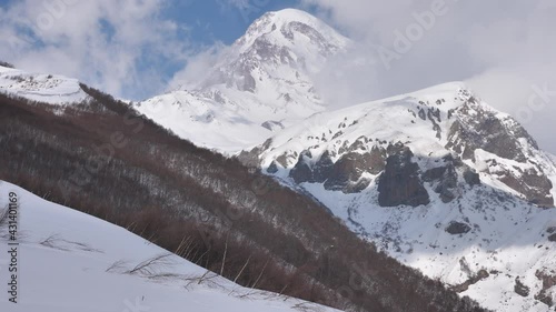 Picturesque rocky landscape of Caucasus mountains with view of snow covered Mount Kazbek in white clouds on sunny spring day, Georgia. High quality 4k footage photo