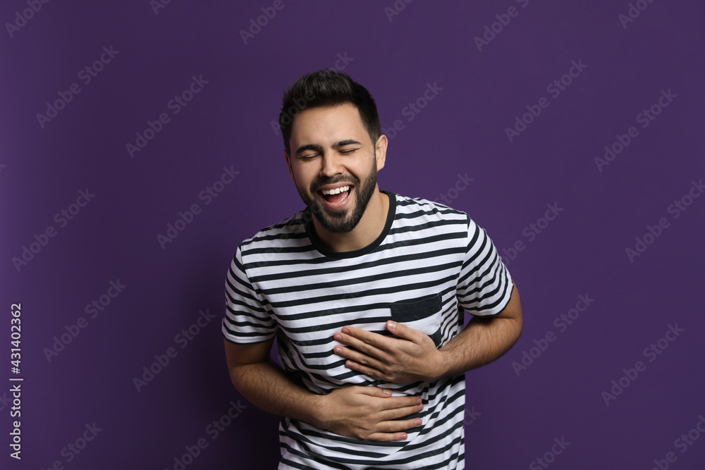 Young man laughing on purple background. Funny joke