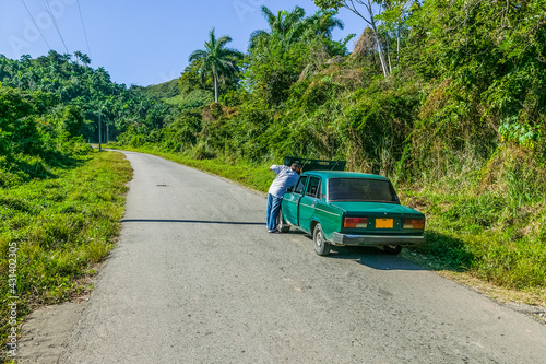 Cuban man with car trouble raising the hood of his car on a lonely deserted road in the Escambray Mountains in Cienfuegos, Cuba.