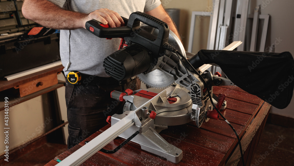 Man cutting aluminum profiles with a miter saw. Carpentry work. Construction of windows and doors for houses. Horizontal image.